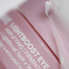 Close-up of a pink label for Solawaves LightBoost Eye Cream, featuring Eye Amplifying/Firming enhanced by LightBoost technology. A glossy, translucent cream is artfully smeared on the surface.