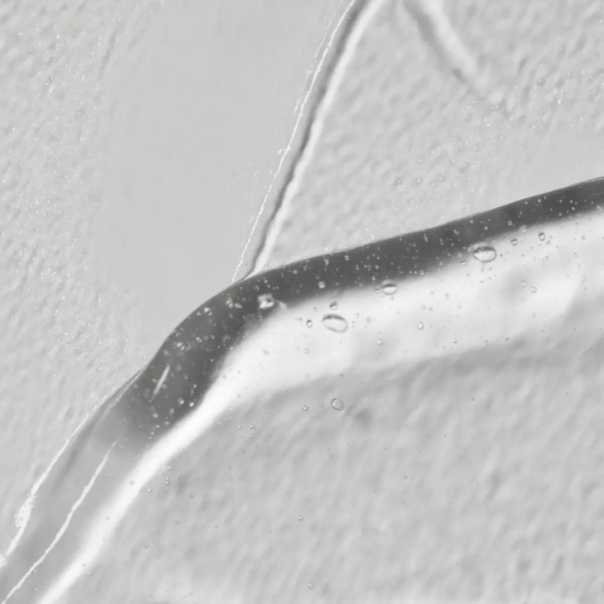 Close-up of a translucent LightBoost Wand Activating Serum in clear gel form with air bubbles on a smooth, light gray background. The glossy, slightly viscous gel highlights Solawaves innovative LightBoost technology for enhanced skincare results.