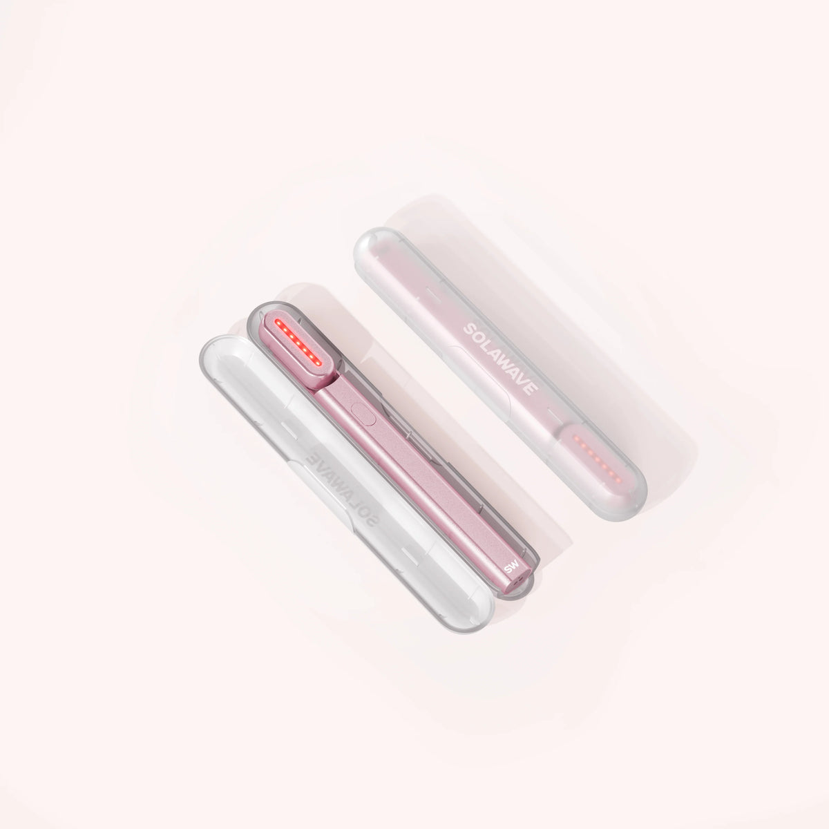 Three Solawave Radiant Renewal Skincare Wands, two white and one pink, feature a sleek cylindrical design with small lights. Positioned diagonally against a light background, they elegantly display the brand name. Ideal for home or travel use with a handy carrying case for convenience. || Clear